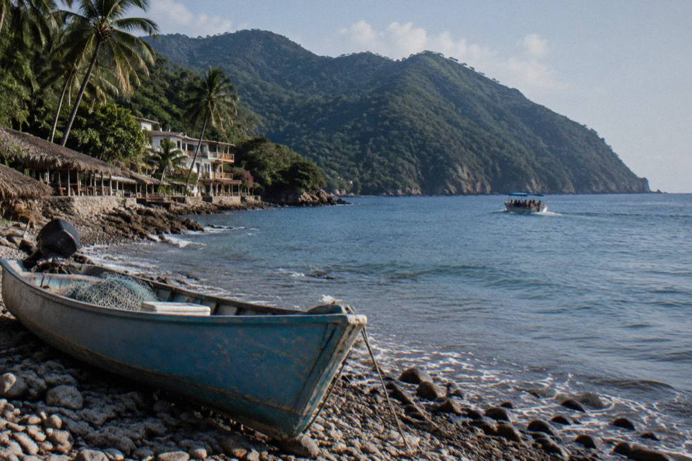 A small tour boat on open blue water with green mountains along a distant shoreline