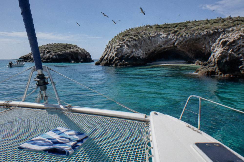 A catamaran anchored in clear water near rocky islands under a bright sky