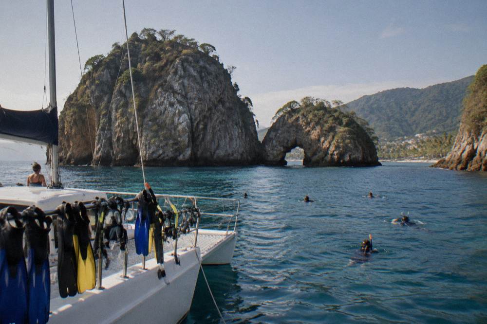 A catamaran anchored near rocky islands with passengers on deck in morning light