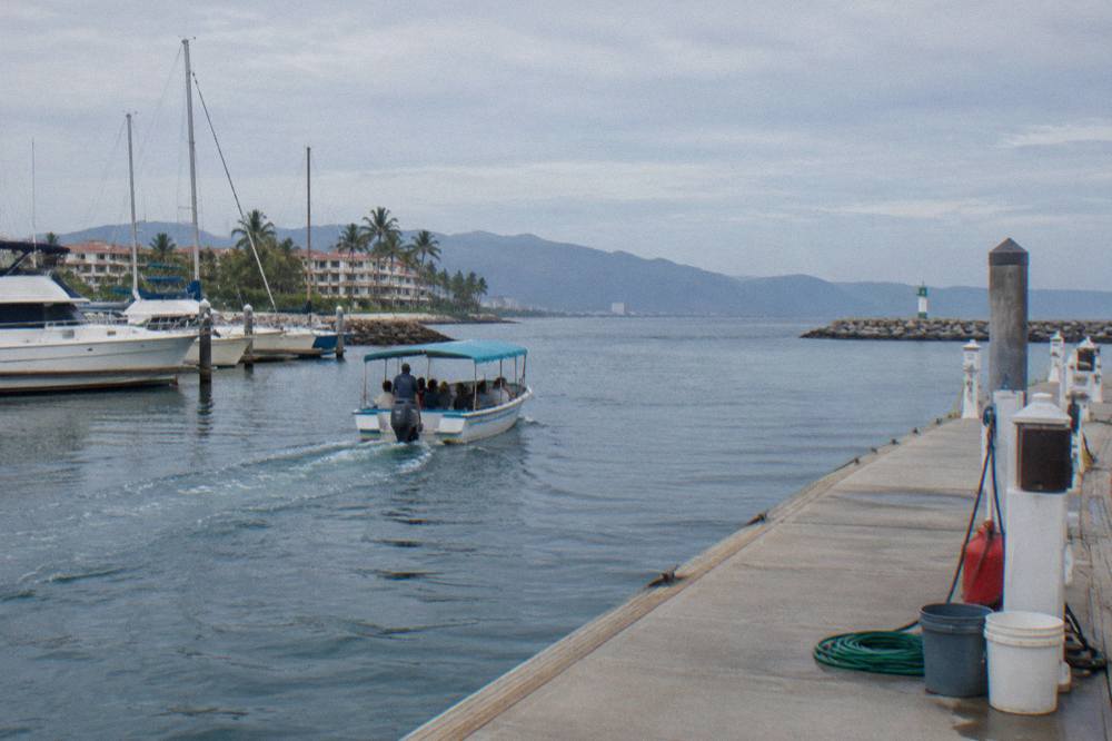 Small tour boat moving slowly across open blue water in a wide Pacific bay