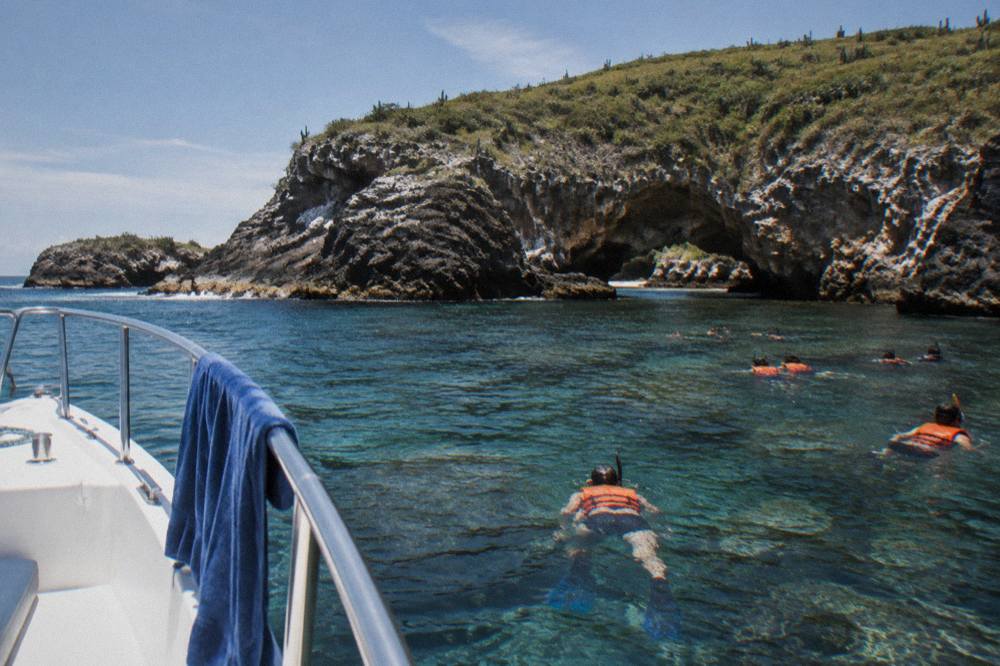 A tour boat anchored near a rocky island with snorkelers entering clear water near a reef
