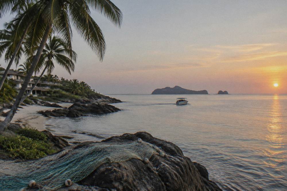 A calm bay morning with a boat underway toward island silhouettes on the horizon