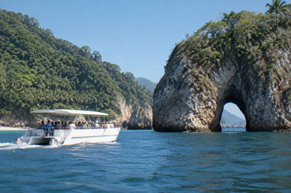 Catamaran with passengers aboard cruising past rocky shoreline under a clear sky