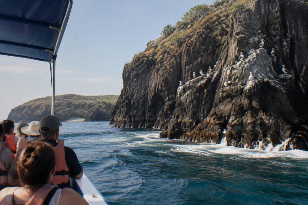 Tour boat anchored near tall rocky cliffs at the edge of an island