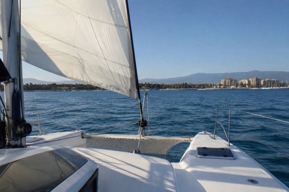 A catamaran under sail on open blue water with hills along a distant coastline