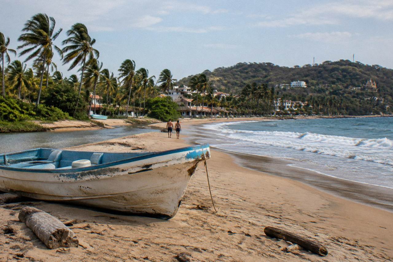 A small boat resting on golden sand beside gentle surf at a beach town on Banderas Bay