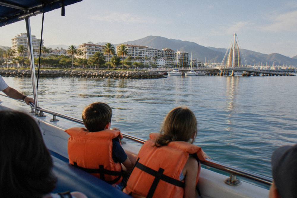 A family with two children wearing orange life jackets seated on a boat deck facing open water