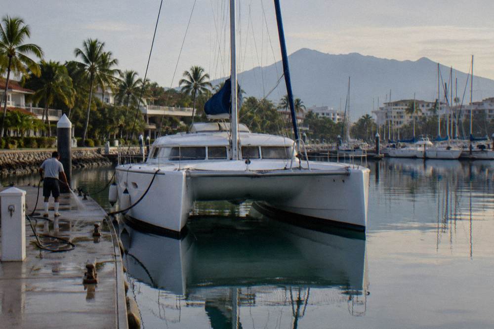 A catamaran moored at a marina dock with mountains behind and calm morning water