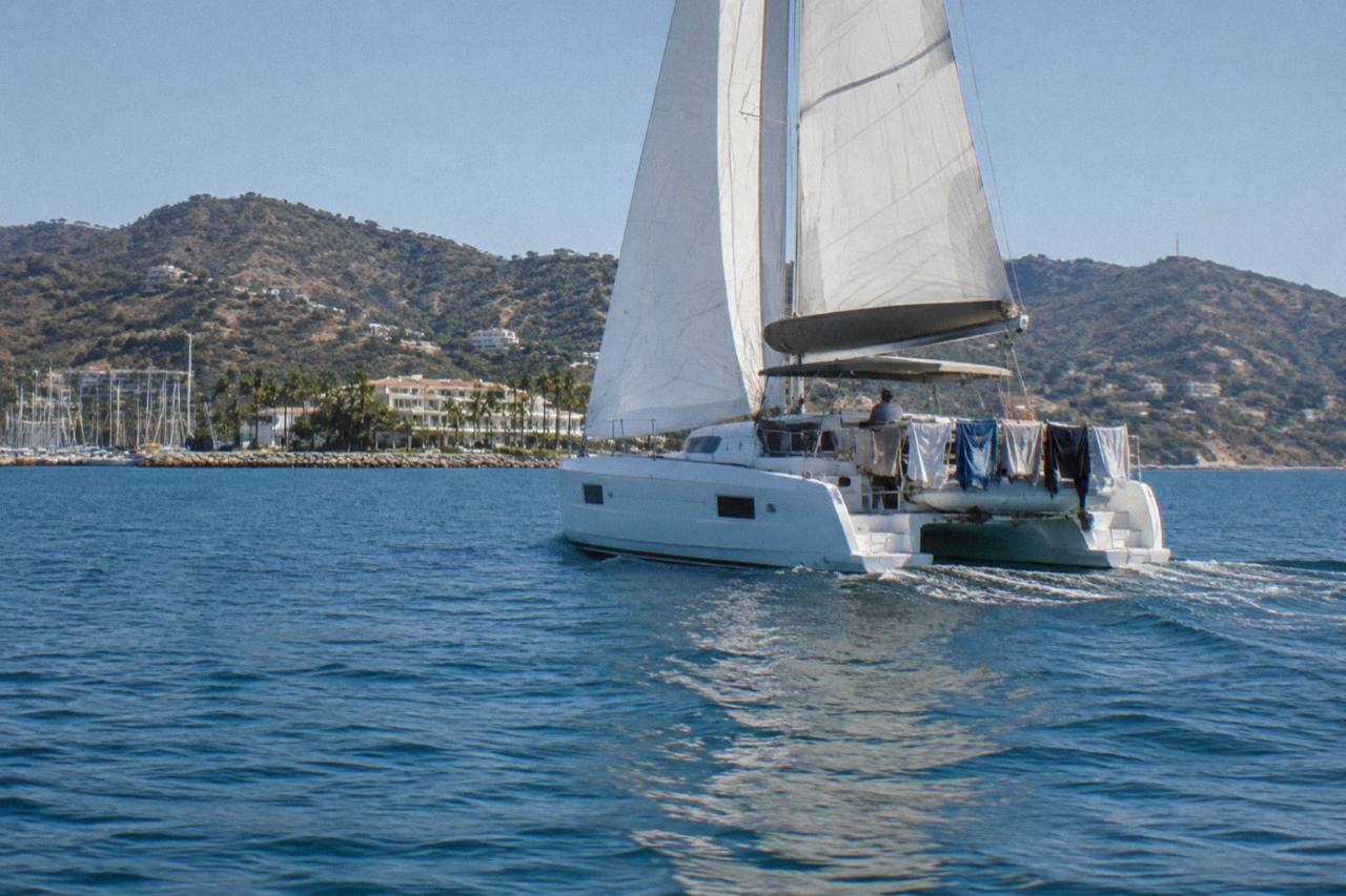 A catamaran under sail on open blue water in Banderas Bay with hilly coastline in the distance
