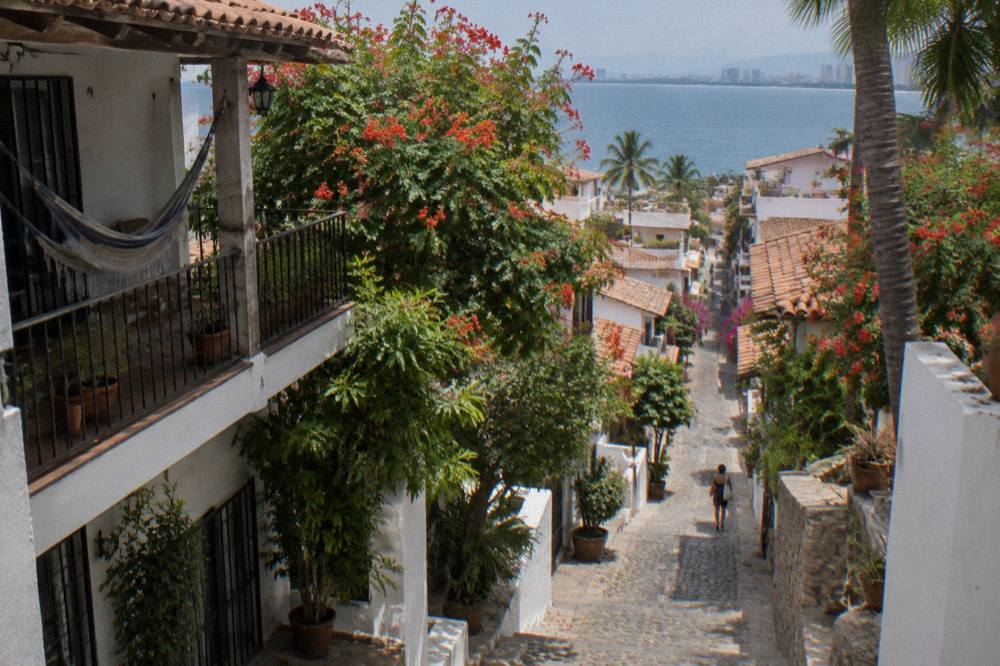 Cobbled street in an old town neighborhood with white buildings, flowering trees and a distant bay