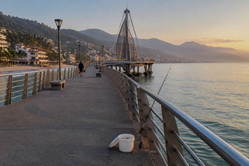Ocean pier extending into a wide calm bay with distant forested headlands
