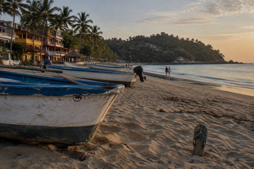 Small surf town beach with fishing boats, colorful buildings and a forested point