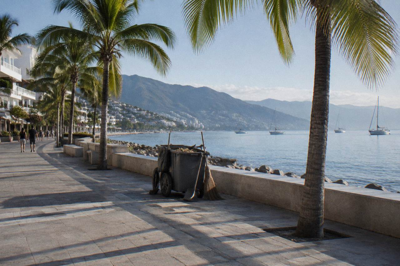 Wide stone boardwalk along Puerto Vallarta harbor with palm trees and boats on calm blue water