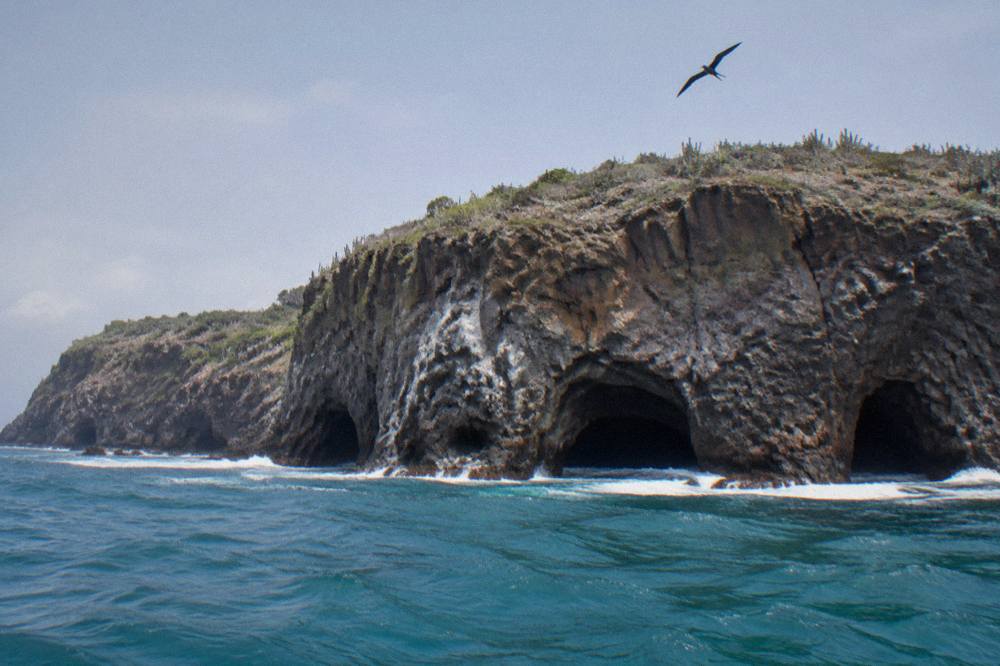 Turquoise water breaking against tall rocky cliffs of a small uninhabited island