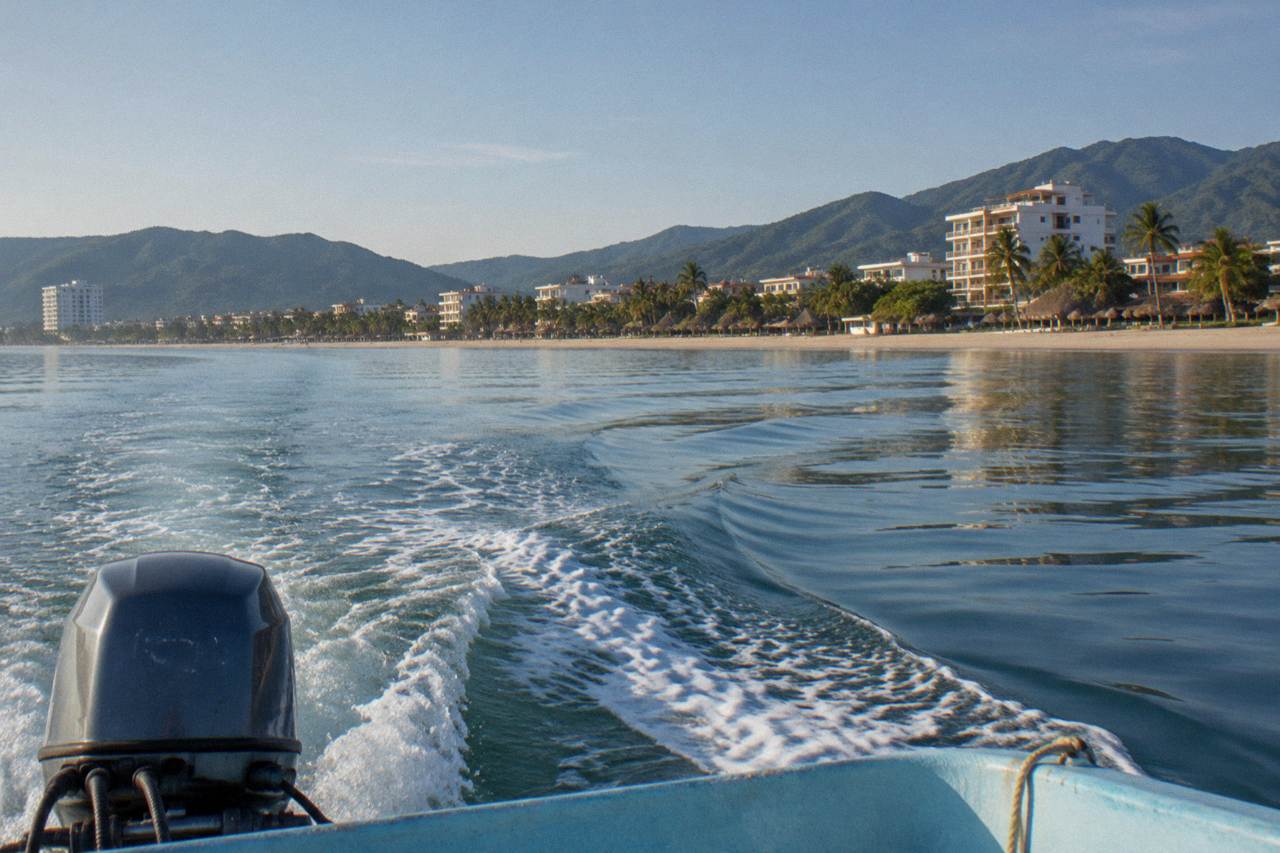 A small whale watching boat cruising across calm open water in Banderas Bay with forested hills on the horizon