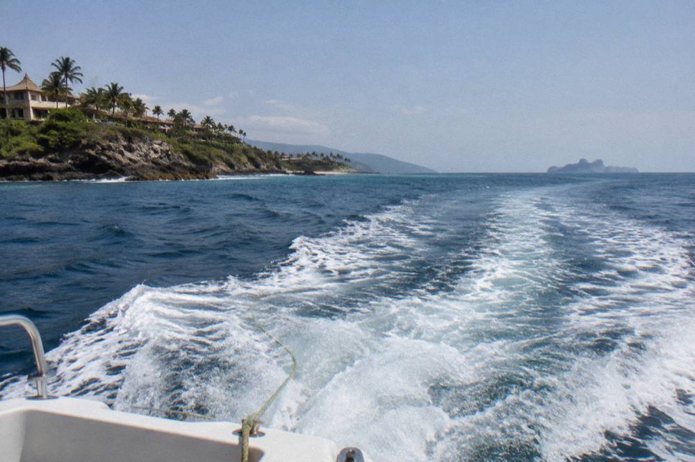 A boat crossing open blue water toward distant rocky islands on the horizon