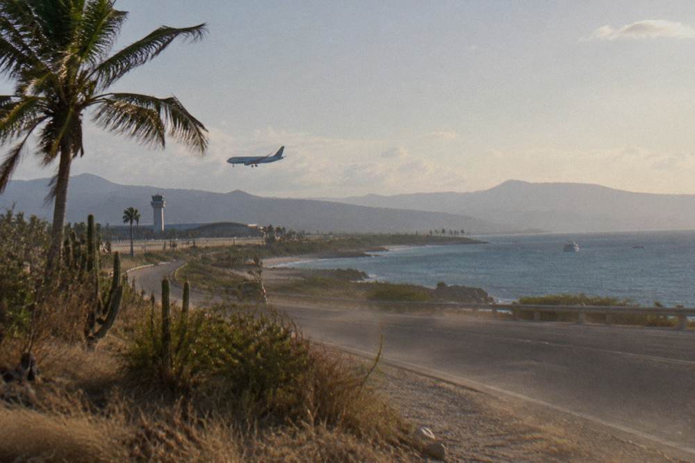 A coastal road curving along a wide bay with boats far offshore