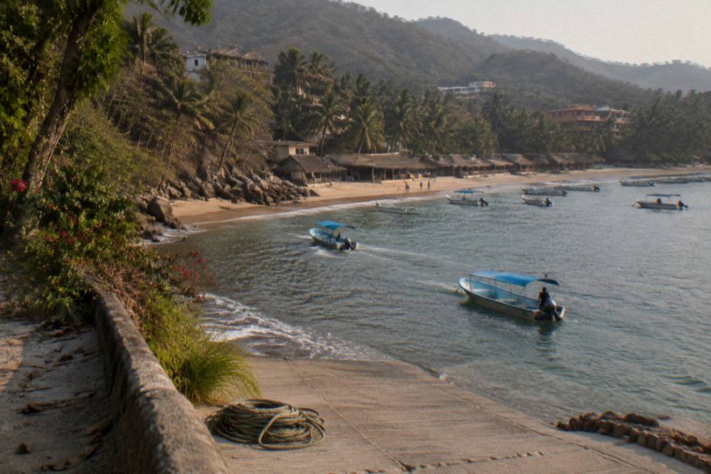 Tour boats anchored near a beach town shoreline with jungle hills behind