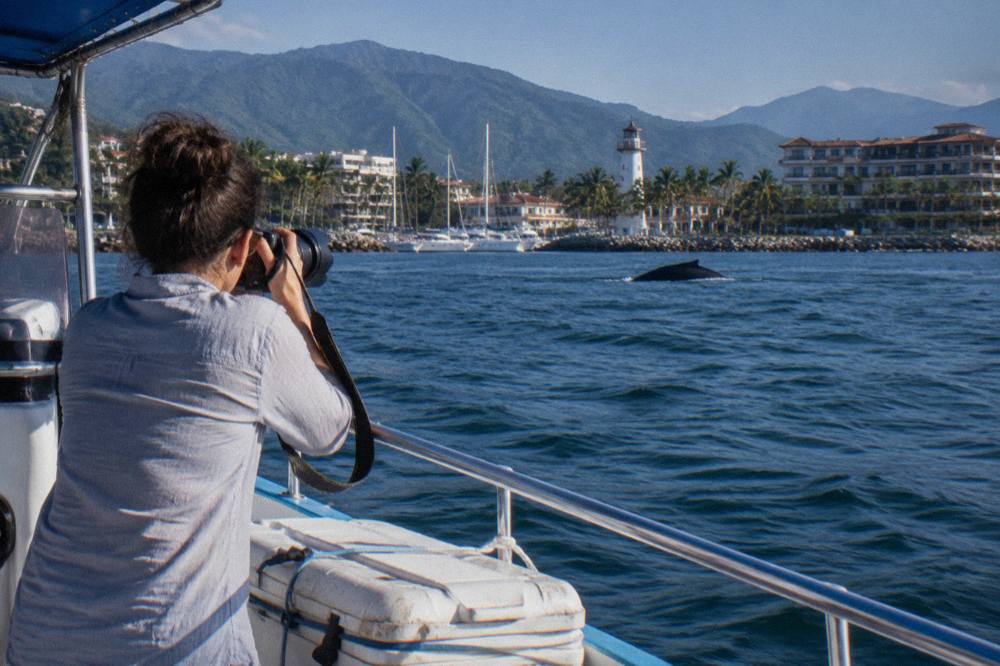 A photographer with a telephoto lens standing at the rail of a small boat on open water