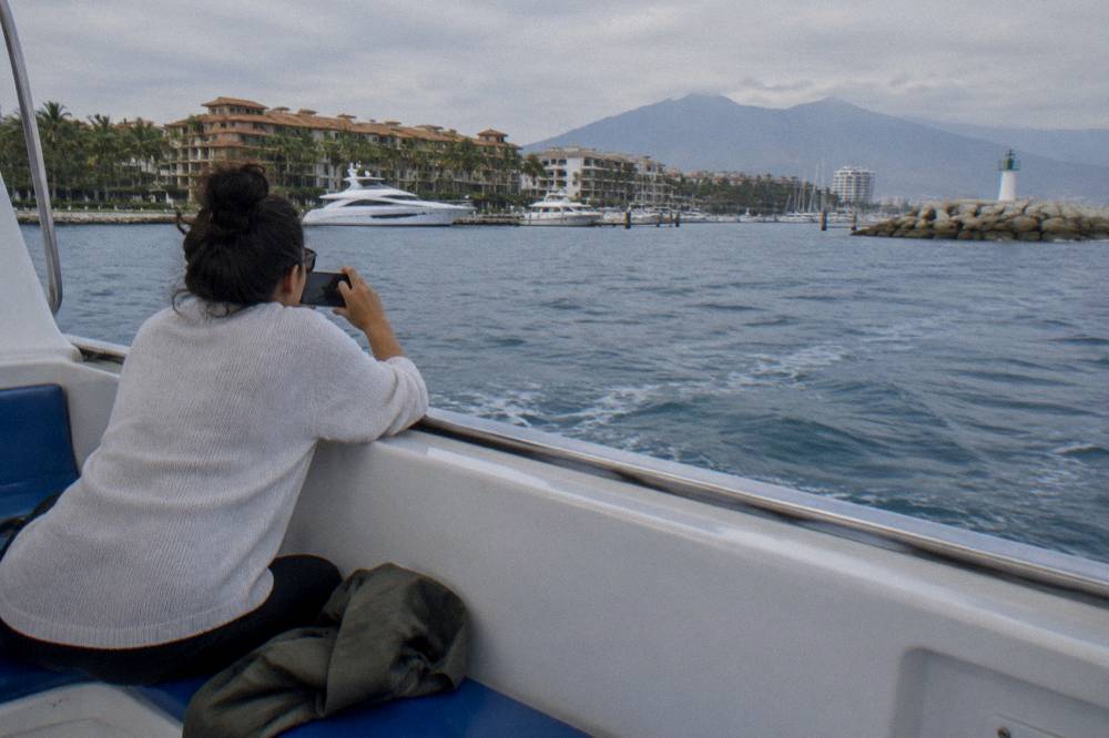 A visitor holding a smartphone toward open water from the deck of a whale watching boat