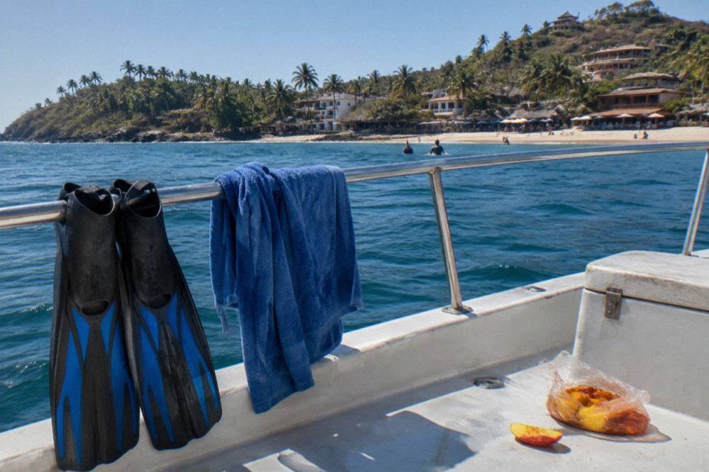 Snorkel fins and a towel drying on the rail of a small tour boat in bright sunlight