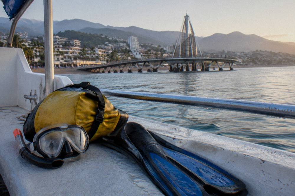 Mask and fins resting on a boat deck beside a dry bag in morning light