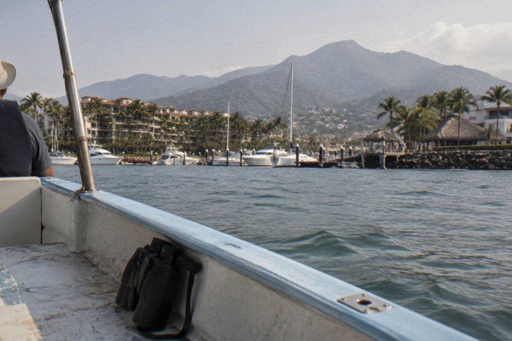 A small whale watching boat on calm blue water in Banderas Bay with hilly coastline behind