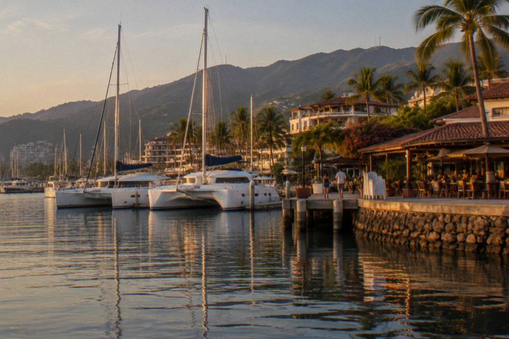 Masts and boats moored in Marina Vallarta at golden hour with restaurants along the dock