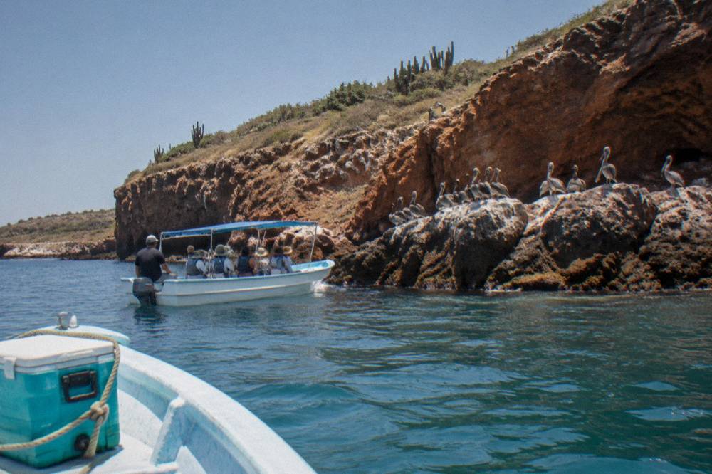 Boats anchored near the rocky shoreline of the Marietas Islands on a clear day