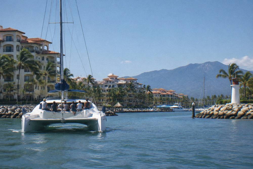 A catamaran departing a marina in Nuevo Vallarta with passengers seated on the net at the bow